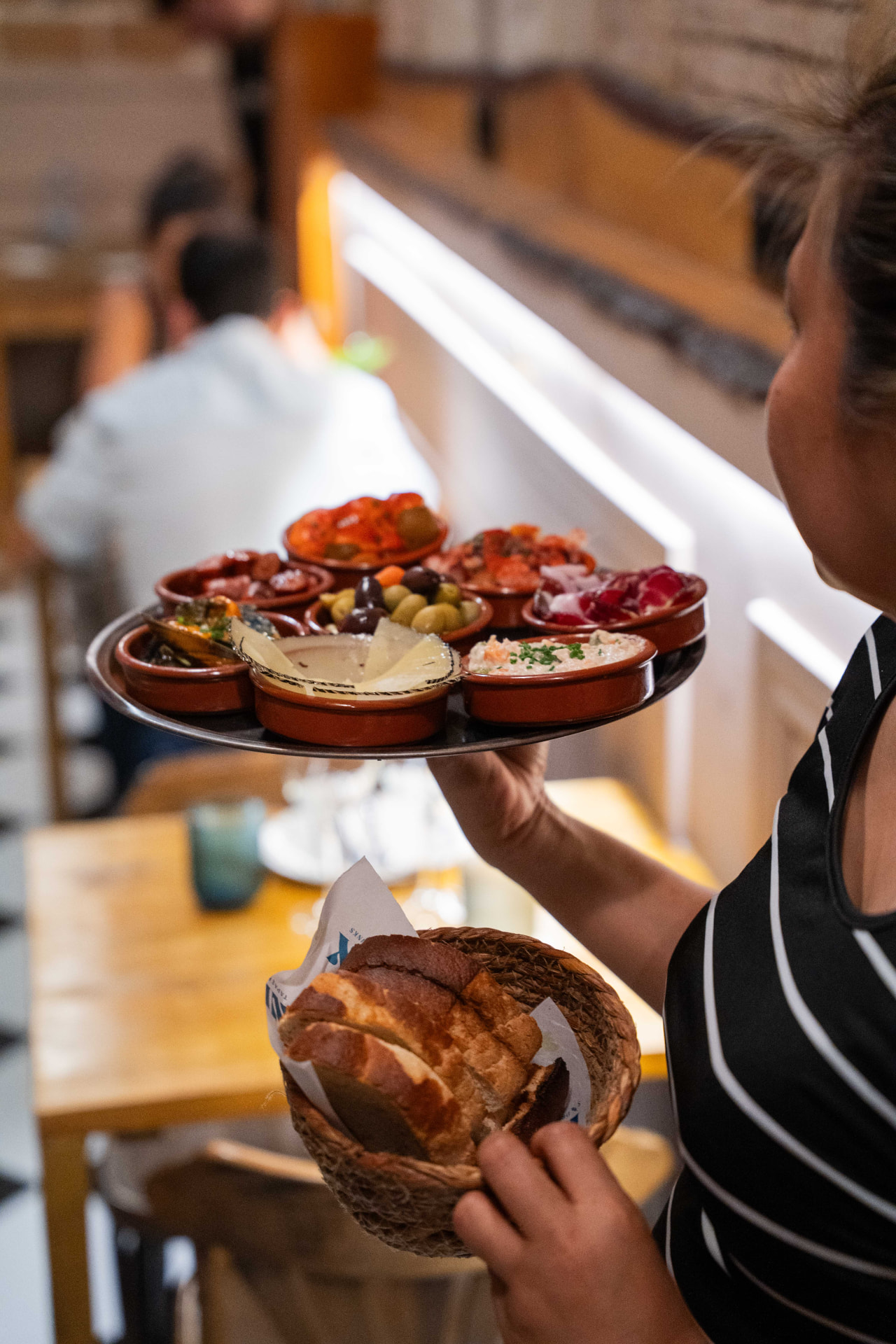 Waitress carrying a full round of tapas and a basket of bread